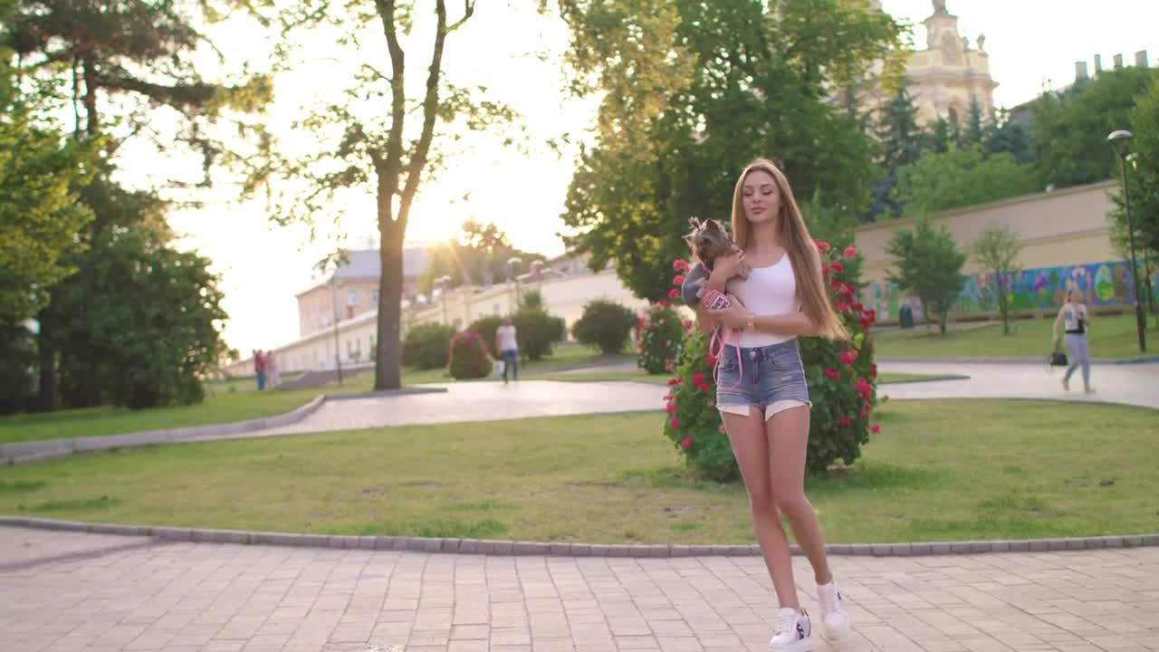 Beautiful Girl Walking With Her Small Dog In The City Park And Using Smartphone