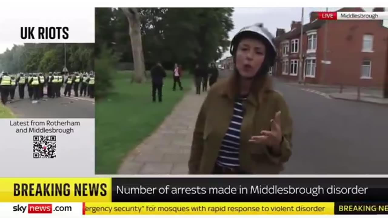 Armed migrants walk behind a reporter as she discusses "far-right" protestors