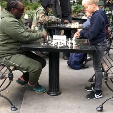 Little boy playing chess in park against man in green track suit