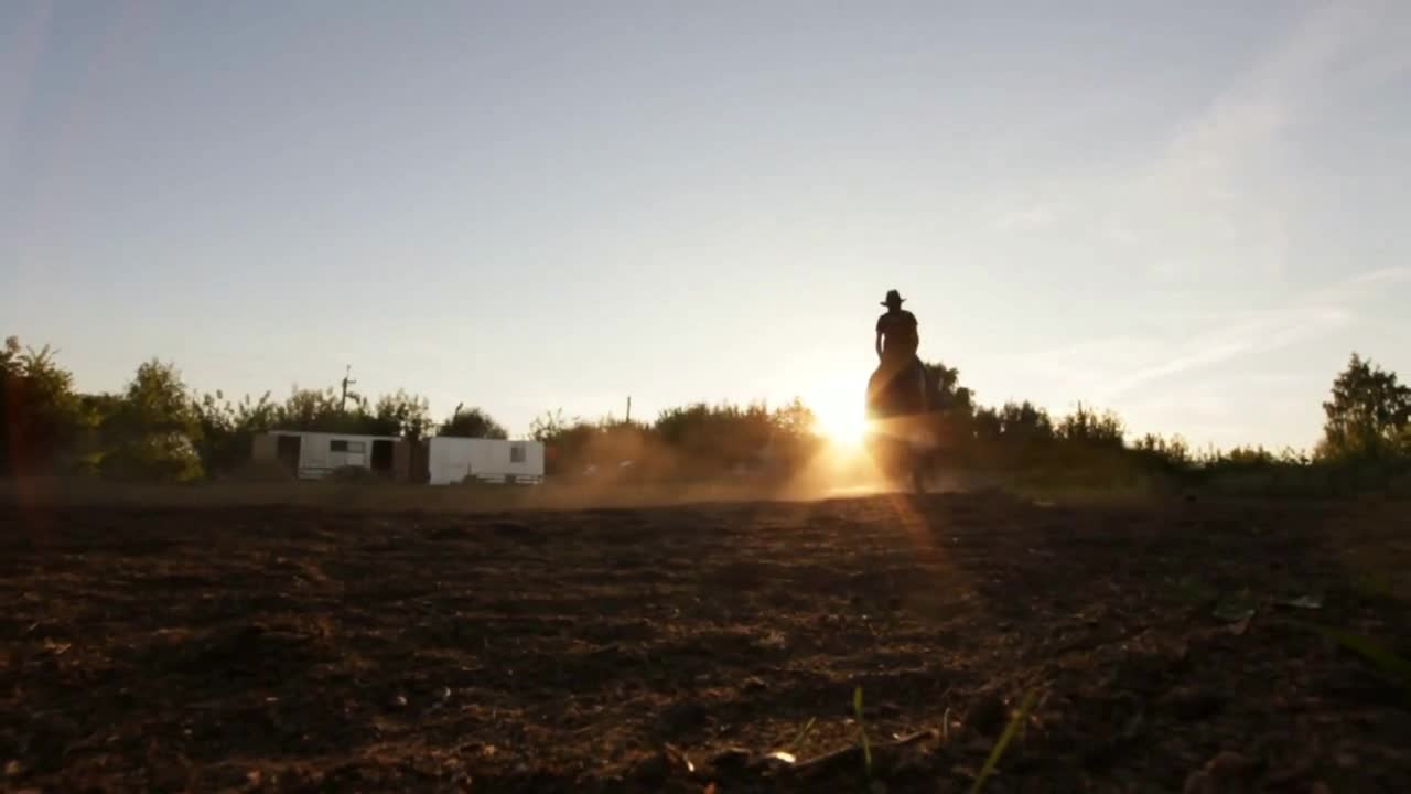 Silhouette shot of a horse rider with dust blowing - sunset, in front of the sun, slow-motion