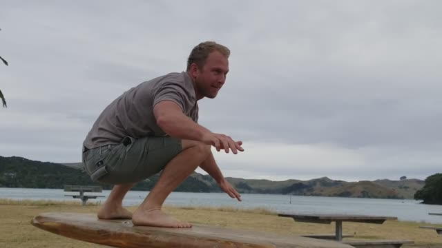 Grey shirt surfboard practices standup on iron pole trainer