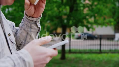 A Man Walks With The Phone And Coffee Cup In The Frame Only Hands Seen-A man walks with the phone an