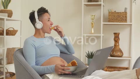 Pregnant Woman Eating Sweets while Watching Movie on Laptop_