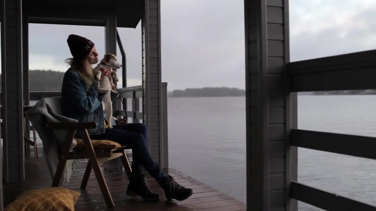 woman with a dog sits on the terrace of a house on the lake