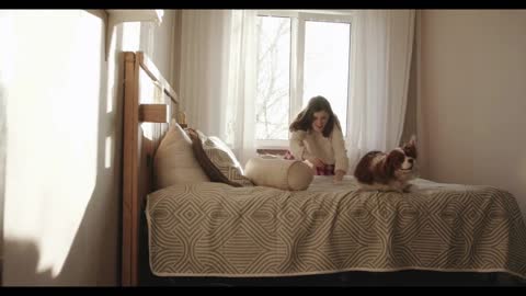 A cheerful young girl plays with her dog while sitting on the bed