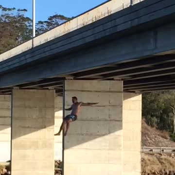 Shirtless man backflips off bridge and back flops in river