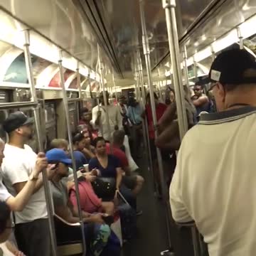 Guy white tank top black shorts upside down dancing on subway train pole