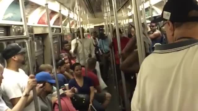 Guy white tank top black shorts upside down dancing on subway train pole