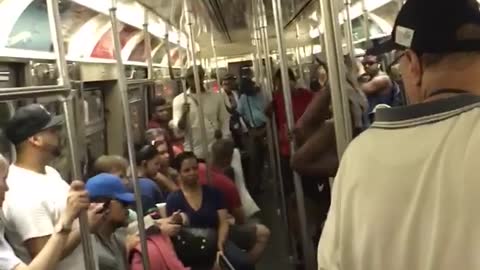 Guy white tank top black shorts upside down dancing on subway train pole