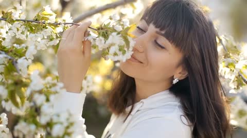 Black haired woman smelling white flowers