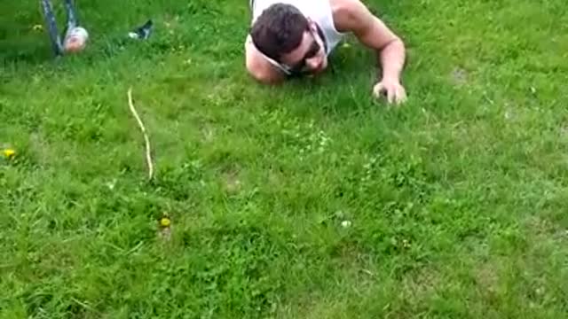 Man in white sleevless shirt and glasses tries to jump over picnic table but racks himself