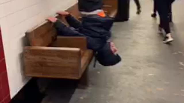 Guy hangs upside down on subway station bench