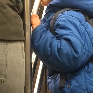 Little boy in blue jacket licks subway rail