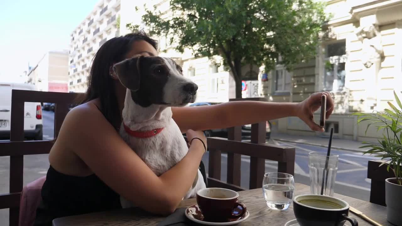 Girl taking selfie with her adorable white and brown dog while having coffee