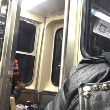 Man in orange and black beanie smokes on the back of subway train