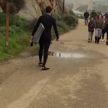 Wet suit flippers guy walks down road with surboard
