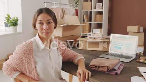 Woman Sitting In Front Of Computer Managing Online Store, Looks At The Camera With A Serious Face