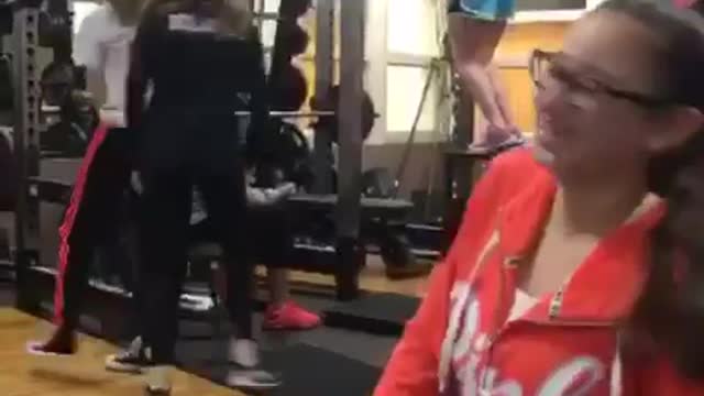 Blue shorts girl tries to hang from squat rack but falls down