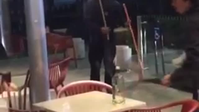 Hooded man at fast food restaurant plays with long wooden dowels like they are swords