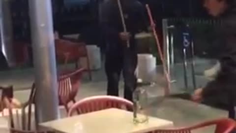 Hooded man at fast food restaurant plays with long wooden dowels like they are swords