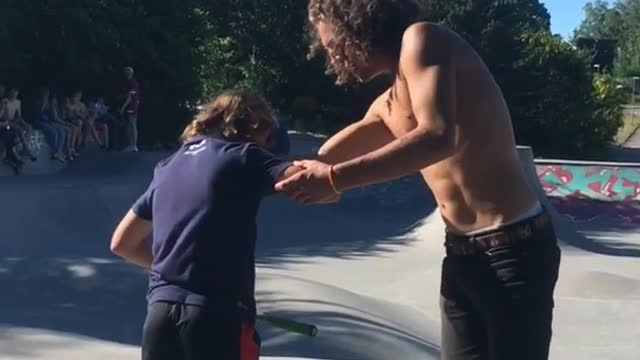 Shirtless curly hair guy kicks up skateboard skateboard hits scooter kid on head