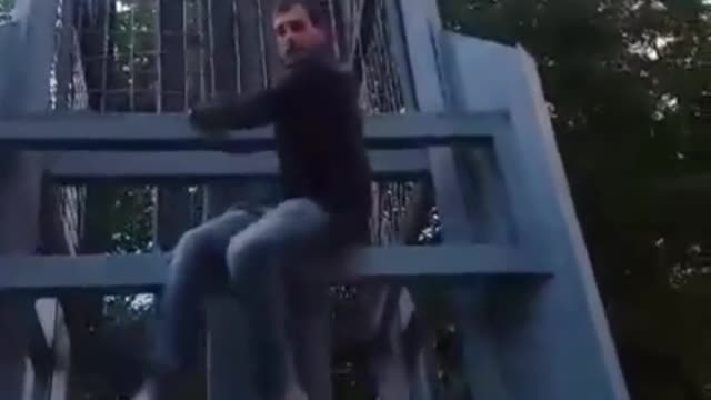 Plaid shirt guy jumps off metal statue falls down