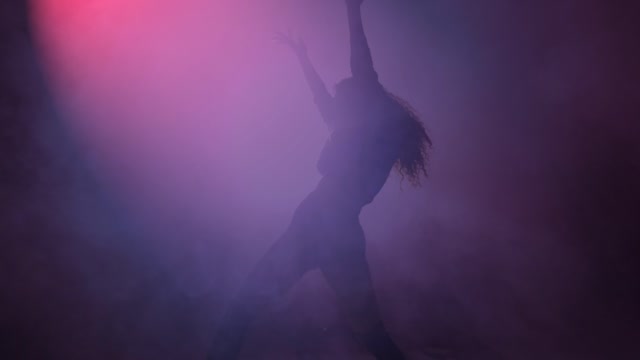 Young woman dancing under a cloud of smoke and a purple light