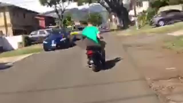 Man in green carrying surf board on moped