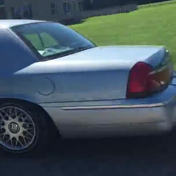 Small blue car tows large white boat down road