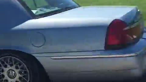 Small blue car tows large white boat down road