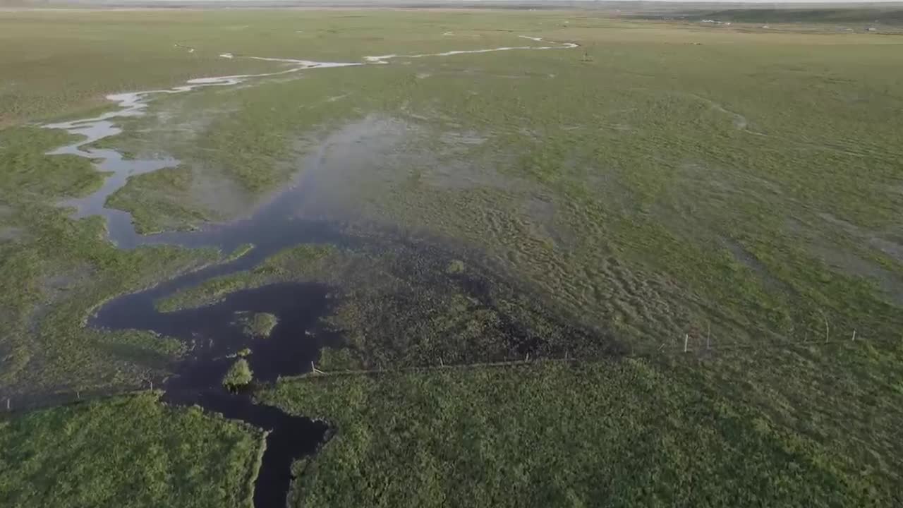 The sun sets on a meandering stream on a vast prairie