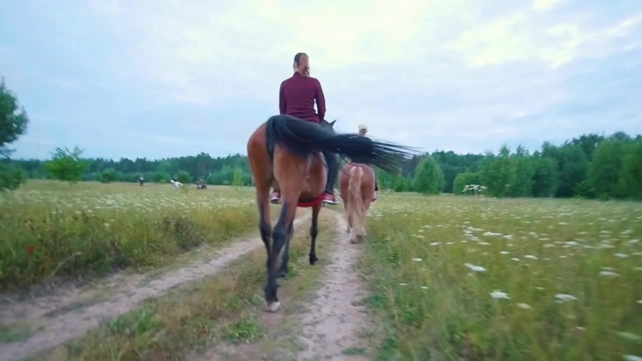 Rear view of female riders on horseback passing by the path