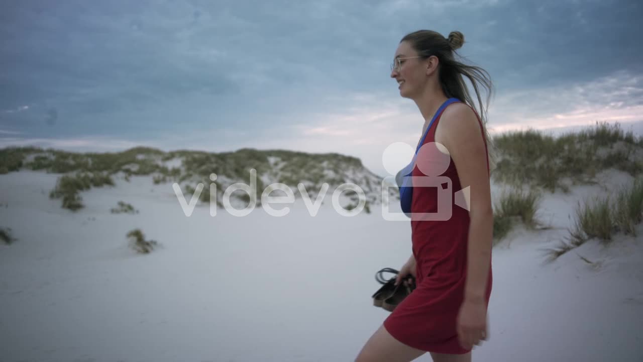 Young woman walks at a white sand beach wearing a red