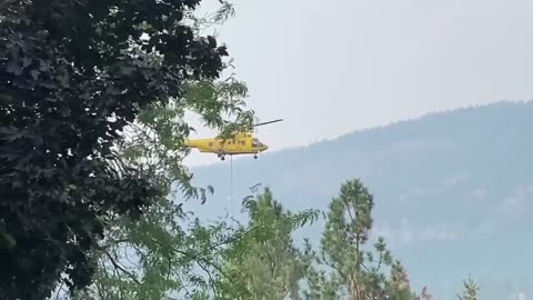 Helicopters fight strong winds while picking up water to fight fire