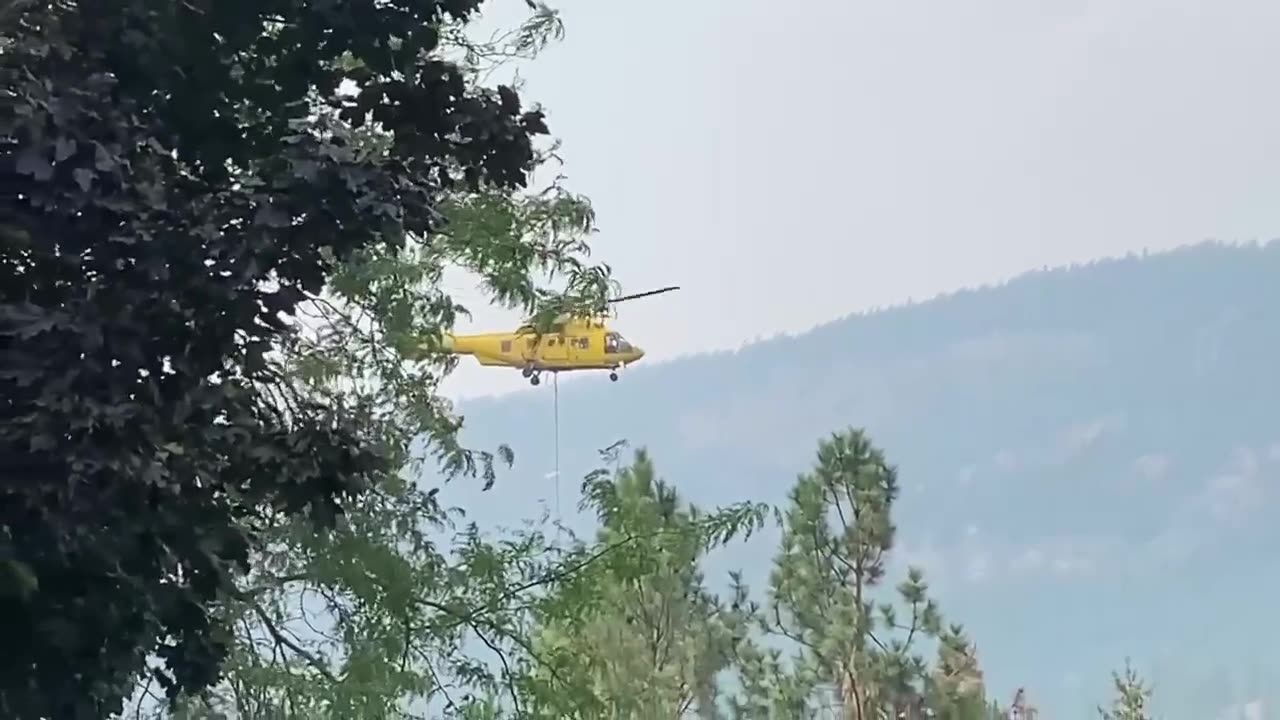 Helicopters fight strong winds while picking up water to fight fire
