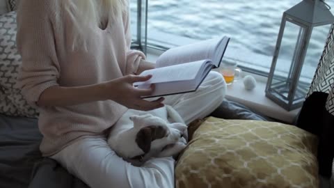 girl with a puppy reading a book sitting by the window with a lake view