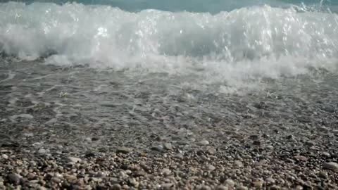 Small sea waves rush onto the shore from small pebbles.