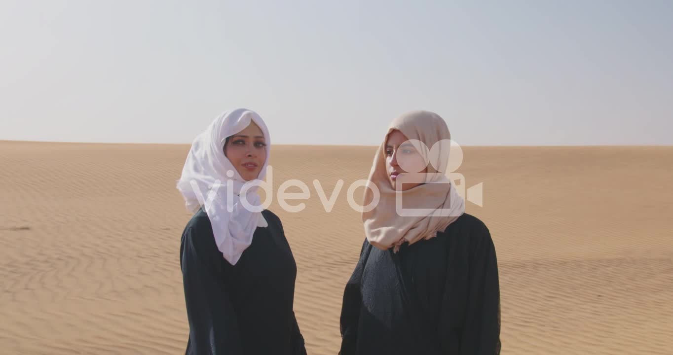 Two Muslim Women Wearing Traditional Dress And Hijab Standing In A Windy Desert 1