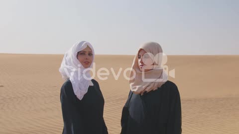 Two Muslim Women Wearing Traditional Dress And Hijab Standing In A Windy Desert 1