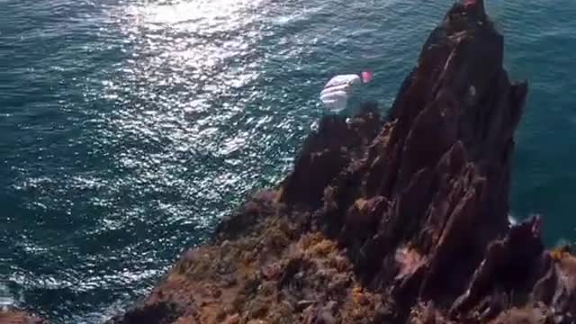 Bird's Eye View Of Man Paragliding From Cliff To Beach