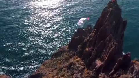 Bird's Eye View Of Man Paragliding From Cliff To Beach