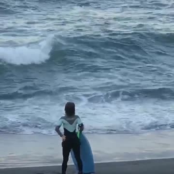 Girl black wet suit dancing on beach sand watching waves