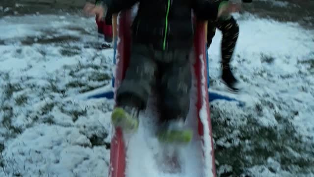 Baby slides down snow covered red slide and stairs at camera