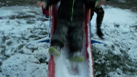 Baby slides down snow covered red slide and stairs at camera