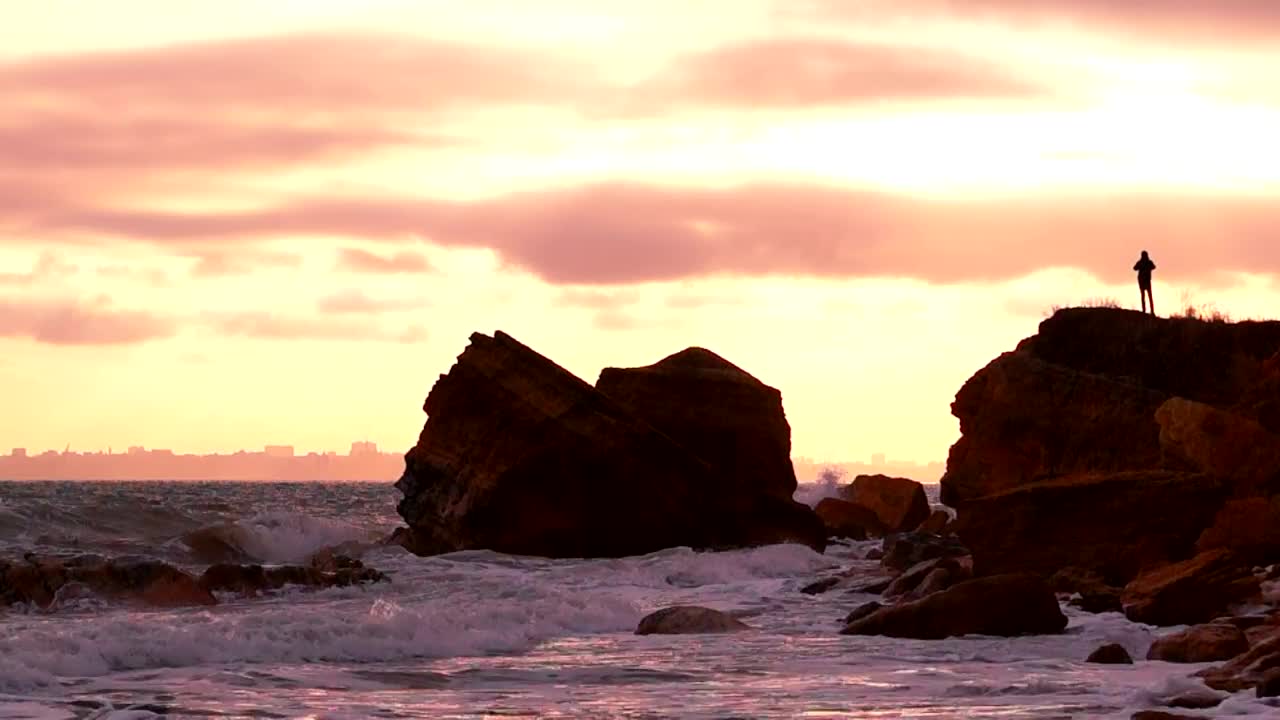 A silhouette of a person over a rock in the seashore at sunset