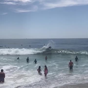 Little girl blue bathing suit gets knocked over by cute wave next to her friend