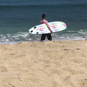 Guy in pink shirt carrying blue surf board