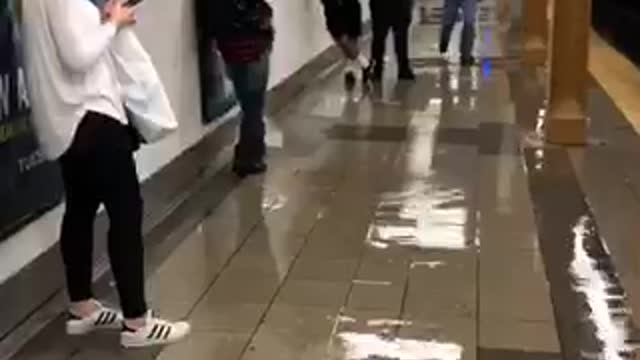 Floor leaking subway station platform guy trying to block hole with foot