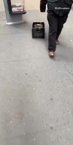 Man drags a milk crate with a string down the sidewalk
