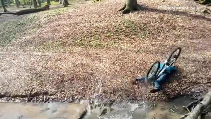 Blue/green sweater boy tries to jump creek in woods but goes over handlebars